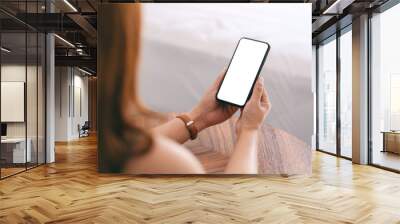 Mockup image of a woman holding and using mobile phone with blank screen while sitting beside the bed Wall mural