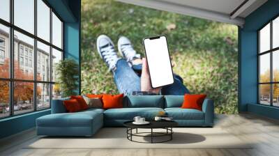 Mockup image of a woman holding black mobile phone with blank white screen while sitting in the outdoors Wall mural