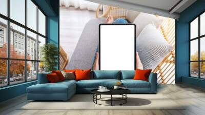 Mockup image of a woman holding black tablet pc with blank desktop white screen while lying on a sofa at home Wall mural