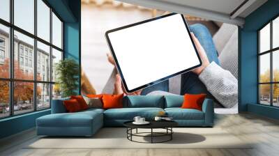 Mockup image of a woman holding black tablet pc with blank desktop white screen while lying on a sofa at home Wall mural