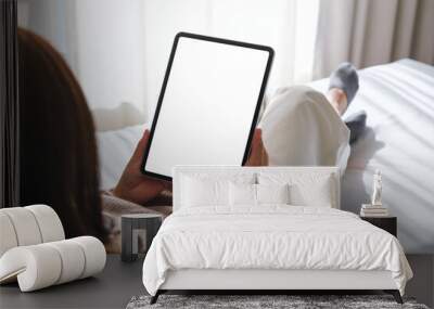 Mockup image of a woman holding digital tablet with blank desktop white screen while laying on a bed Wall mural