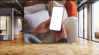 Mockup image of a woman holding mobile phone with blank desktop white screen whilesitting on a sofa at home Wall mural