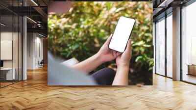 Mockup image of a woman holding mobile phone with blank white desktop screen in the outdoors Wall mural