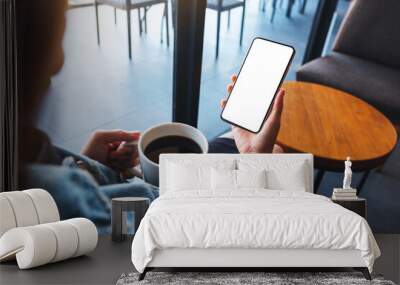 Mockup image of a woman holding mobile phone with blank white desktop screen while drinking coffee Wall mural