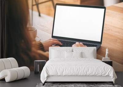 Mockup image of a woman using and typing on laptop computer keyboard with blank white desktop screen with coffee cup on wooden table Wall mural