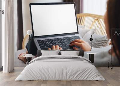 Mockup image of a woman working and typing on laptop computer with blank screen while sitting on a sofa at home Wall mural