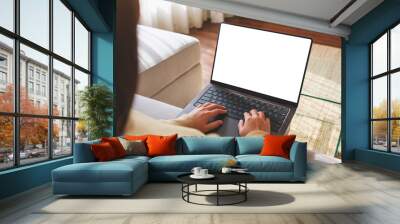 Mockup image of a woman working and typing on laptop computer with blank screen while sitting on sofa at home Wall mural