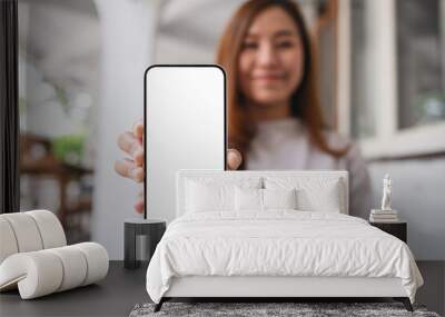 Mockup image of a young woman holding and showing a mobile phone with blank white screen Wall mural