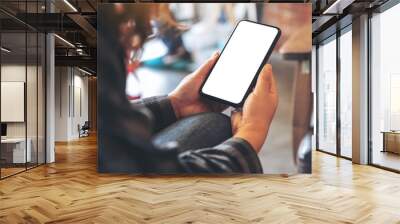 Mockup image of hands holding black mobile phone with blank white desktop screen in cafe Wall mural