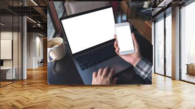 Mockup top view image of business woman holding white mobile phone with blank screen with laptop and coffee cup on wooden table in cafe Wall mural