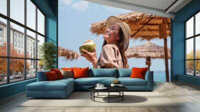 Portrait image of a beautiful asian woman holding a fresh coconut and enjoying on the beach Wall mural