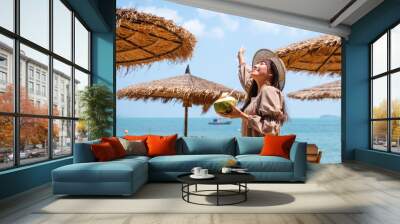 Portrait image of a beautiful asian woman holding a fresh coconut and enjoying on the beach Wall mural