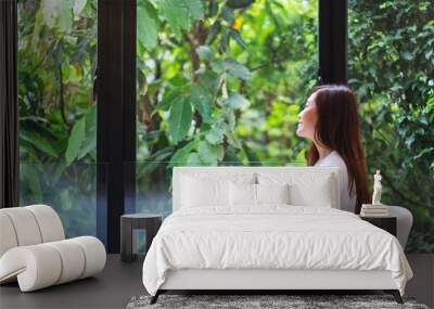 Portrait image of a beautiful asian woman sitting and looking at a green nature outside the window Wall mural