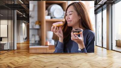 Portrait image of a beautiful young asian woman holding and enjoyed eating donuts at home Wall mural