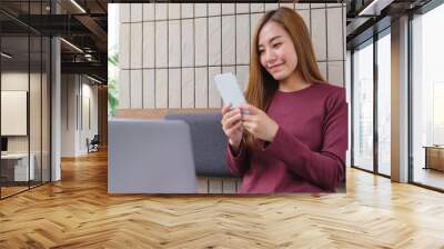 Portrait image of a young woman holding and using smart phone and laptop computer in office Wall mural