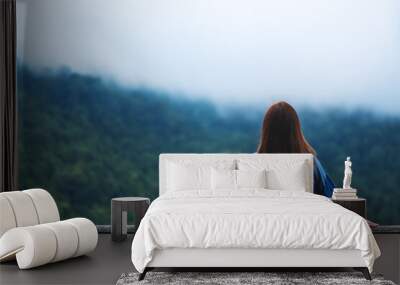 Rear view image of a female traveler looking at a beautiful green mountain on foggy day Wall mural