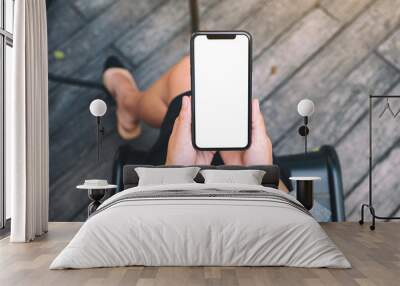 Top view mockup image of a woman holding a black mobile phone with blank white desktop screen Wall mural