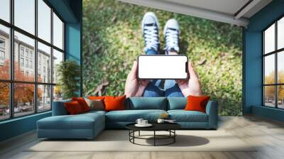 Top view mockup image of a woman holding black mobile phone with blank white screen while sitting in the outdoors Wall mural