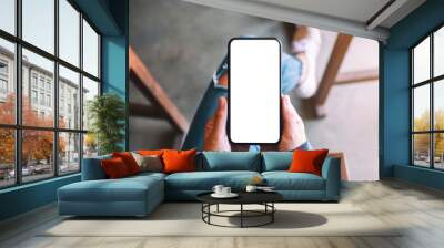 top view mockup image of a woman holding black mobile phone with blank white screen while sitting in Wall mural