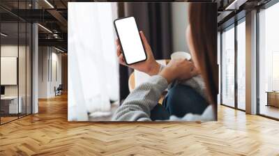 Top view mockup image of a woman holding mobile phone with blank desktop screen while sitting in bed room at home Wall mural