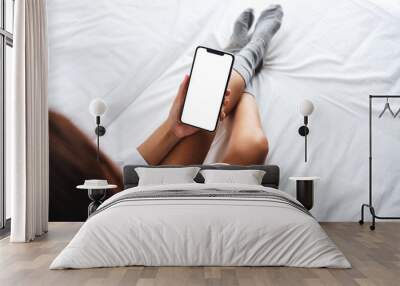 Top view mockup image of a woman holding white mobile phone with blank desktop screen while drinking coffee on a cozy white bed at home in the morning Wall mural