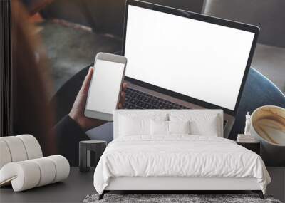 Top view mockup image of hands holding blank mobile phone while using laptop with blank white desktop screen on table Wall mural