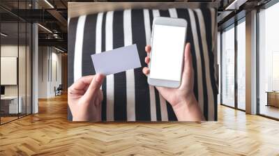 Top view mockup image of hands holding white mobile phone with blank desktop screen and a white empty business card Wall mural