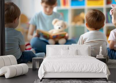 A childcare provider reading a book to a group of young children sitting on a carpet in a bright, colorful room filled with toys. Wall mural