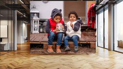 African American boy and girl are sitting on wooden pallets, playing with a Christmas snow globe Wall mural