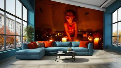 Small child sits in the dark blowing out the candles among the Halloween decorations at home. Wall mural