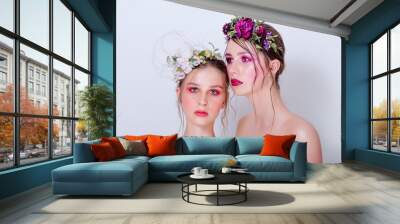 Two fashion beauty models sister girls with professional bright make-up, a hoop of fresh spring flowers on their heads, with red lilac lipstick are posing against a gray uniform background. Clean skin Wall mural