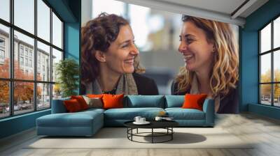 Two women in a cheerful office meeting, one smiling warmly at the other. Wall mural