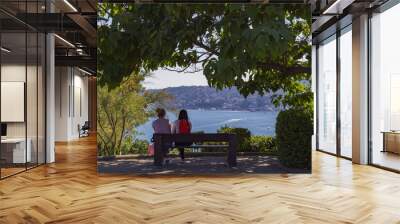 Friends sitting on the wooden bench and looking at the sea Wall mural