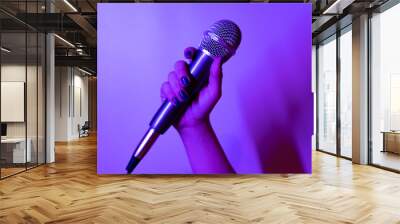 close-up shot of a hand holding a microphone in purple and pink lights Wall mural