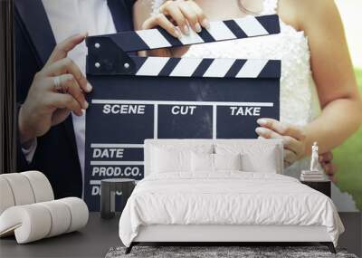 Happy beautiful bride and groom, woman holds clapper board, cinema board  Wall mural