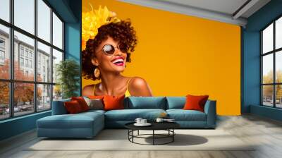 portrait of a smiling african american woman, wearing glasses, flowers on her head, dressed in yellow, isolated on a yellow background Wall mural