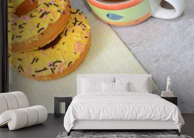 Two yellow donuts are on a napkin and a cup is next to it. Wall mural