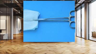 one sterile closed iron industrial hemostatic pure silver shiny with clips surgical clamp with gauze white pad lies on blue table in operating room Wall mural