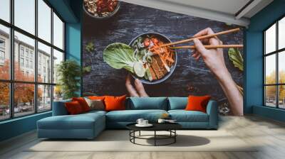 Eating delicious asian bowl with rice noodles, vegetables and tofu on wooden background. Top view Wall mural