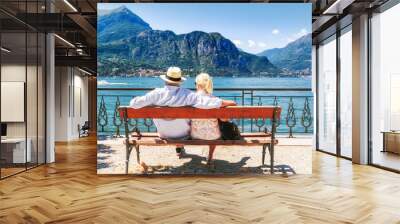 Lake Como, village Bellagio, Italy. Senior couple weekend getaway having rest on the bench by spectacular lake Como in Italy. Sunny day scenery. Tourists admiring view on popular tourist attraction. Wall mural