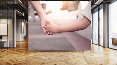 A parent holds the hand of a small boy in the sunset. Wall mural