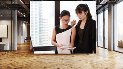 2 asian employees of a company are updating some information with smiling and laughing face from tablet  before working in the morning Wall mural