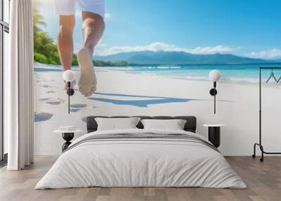 A serene beach scene featuring a person walking barefoot along the shoreline, leaving footprints in soft white sand under a clear sky. Wall mural