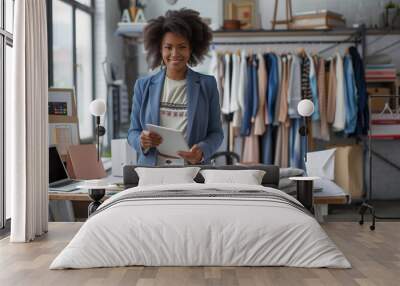 A smiling young entrepreneur holds a tablet in her stylish new clothing boutique, symbolizing the excitement and potential of starting a new business venture. Wall mural