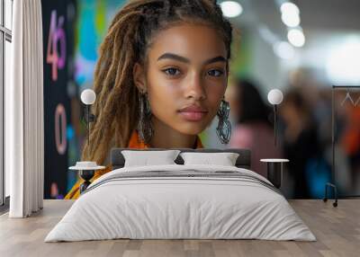 A young woman with stylish dreadlocks wearing an orange shirt, posed against a colorful backdrop, exuding confidence and charm. Wall mural