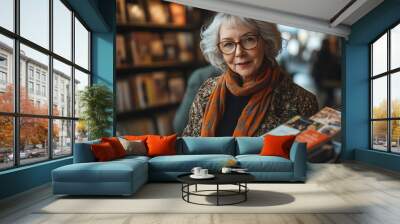 Charming elderly woman with glasses poses in a cozy bookstore filled with books, radiating warmth and wisdom. Wall mural