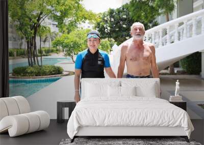 happy elderly caucasian husband and elderly asian wife holding hand while walking to swimming pool in the hotel on hot path and hot weather on sunny day outdoor Wall mural