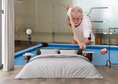 Indoor shot attractive bearded senior caucasian man in white shirt looking and playing billiard or snooker ball with concentration and serious face during the game in sport club. (Focus on his hand) Wall mural