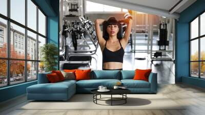 sporty caucasian girl in black sport wear posing for portrait with sexy eyes and body sitting exercise machine in gym Wall mural