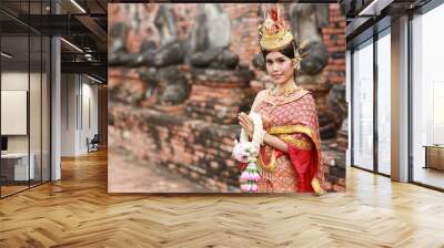 Young fashion and beautiful asian woman in red Thai traditional costume pay respect sawasdee symbol while holding jasmine garland standing in ancient buddha temple Ayutthaya, Thailand. Travel concept Wall mural